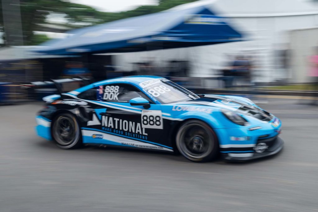 Porsche GT3 Cup race car branded with National Make Good Solutions livery speeding on track during a motorsport event.
