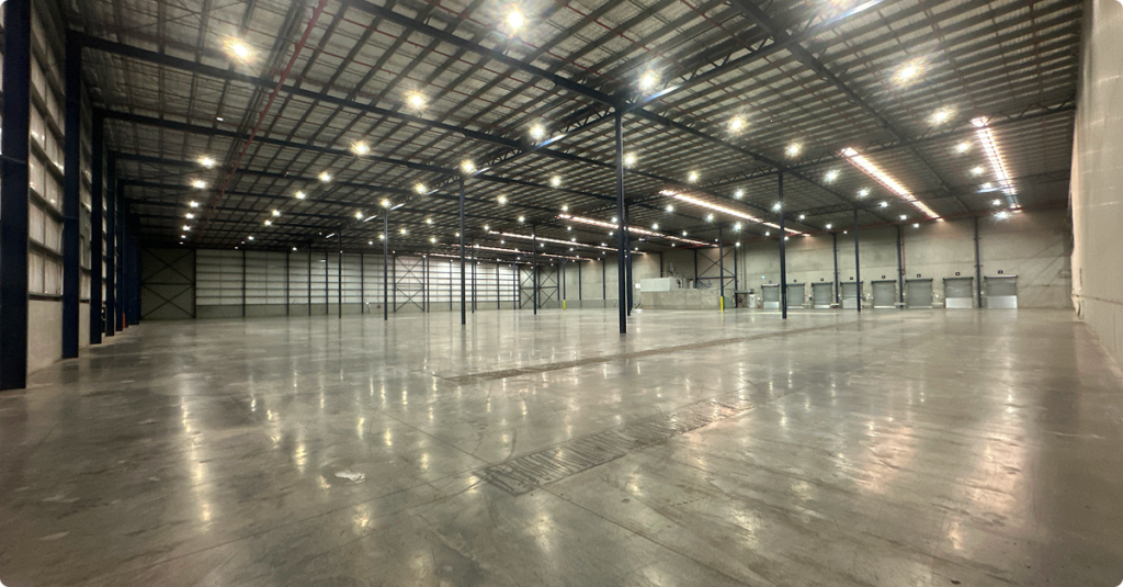Empty large-scale warehouse interior in Scoresby, Victoria, with polished concrete floors, high ceilings, and industrial lighting, following demolition and make-good works for Penguin Random House site decommissioning.